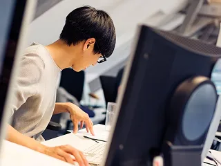 作業着を着てデスクでCAD画面を確認する社員